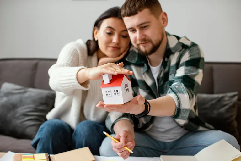 Pareja sentada en un sillón observando una maqueta de casa